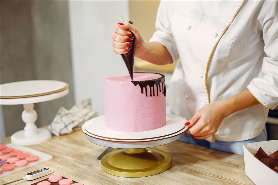 Pastelera decorando una torta rosa con chocolate